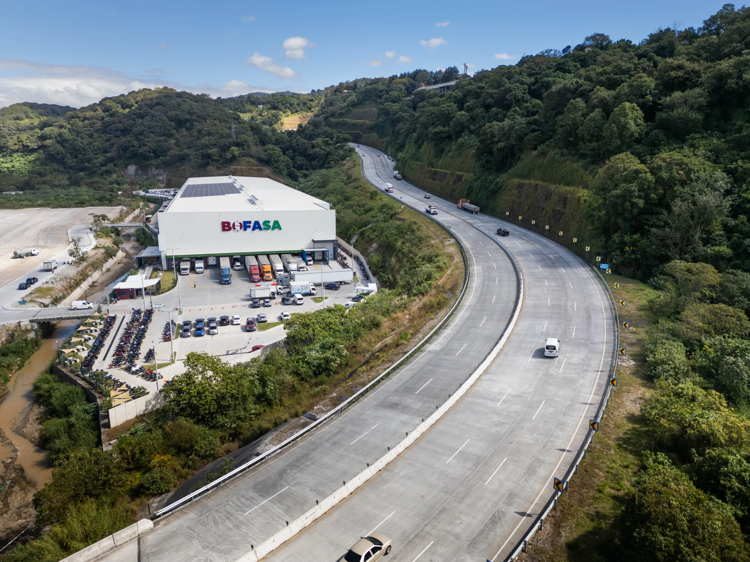 Vista aérea de un tramo vial operado por Cipreses y Pinos junto a un centro de servicios